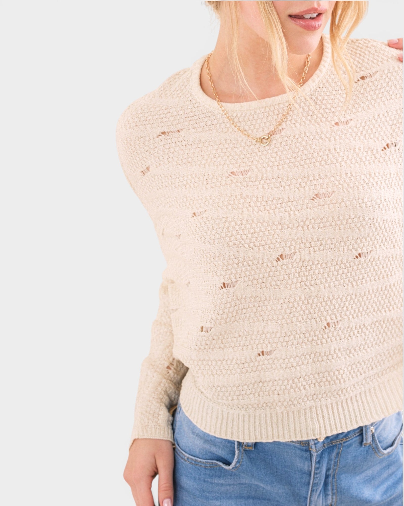 Beige sweater with subtle pattern worn by a person on a light gray background