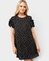 Woman wearing a black dress with white polka dots on a plain background