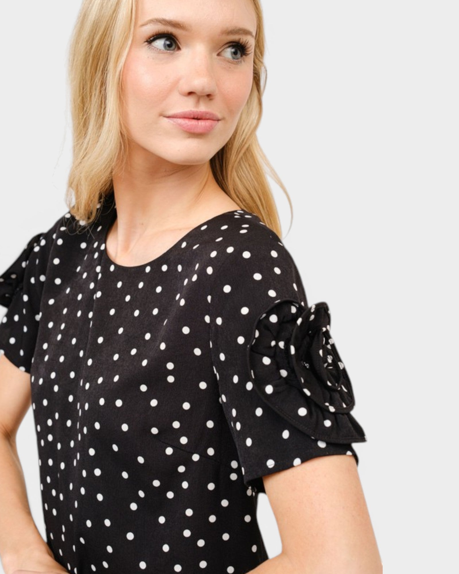 Woman wearing a black polka dot dress with ruffled sleeves on a light gray background