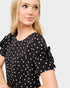 Woman wearing a black polka dot dress with ruffled sleeves on a light gray background