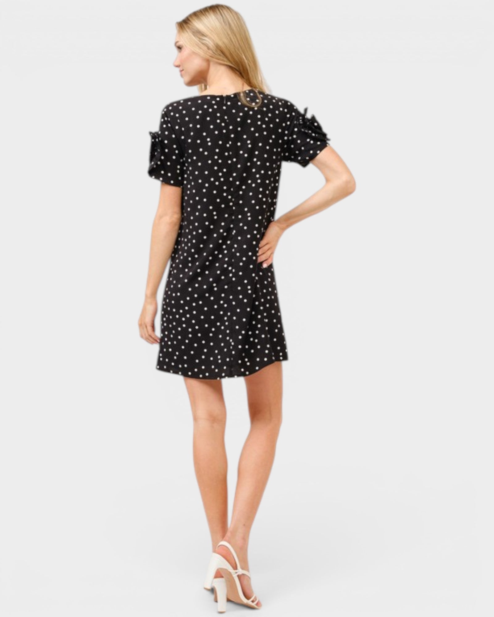 Woman wearing a black dress with white polka dots on a light gray background