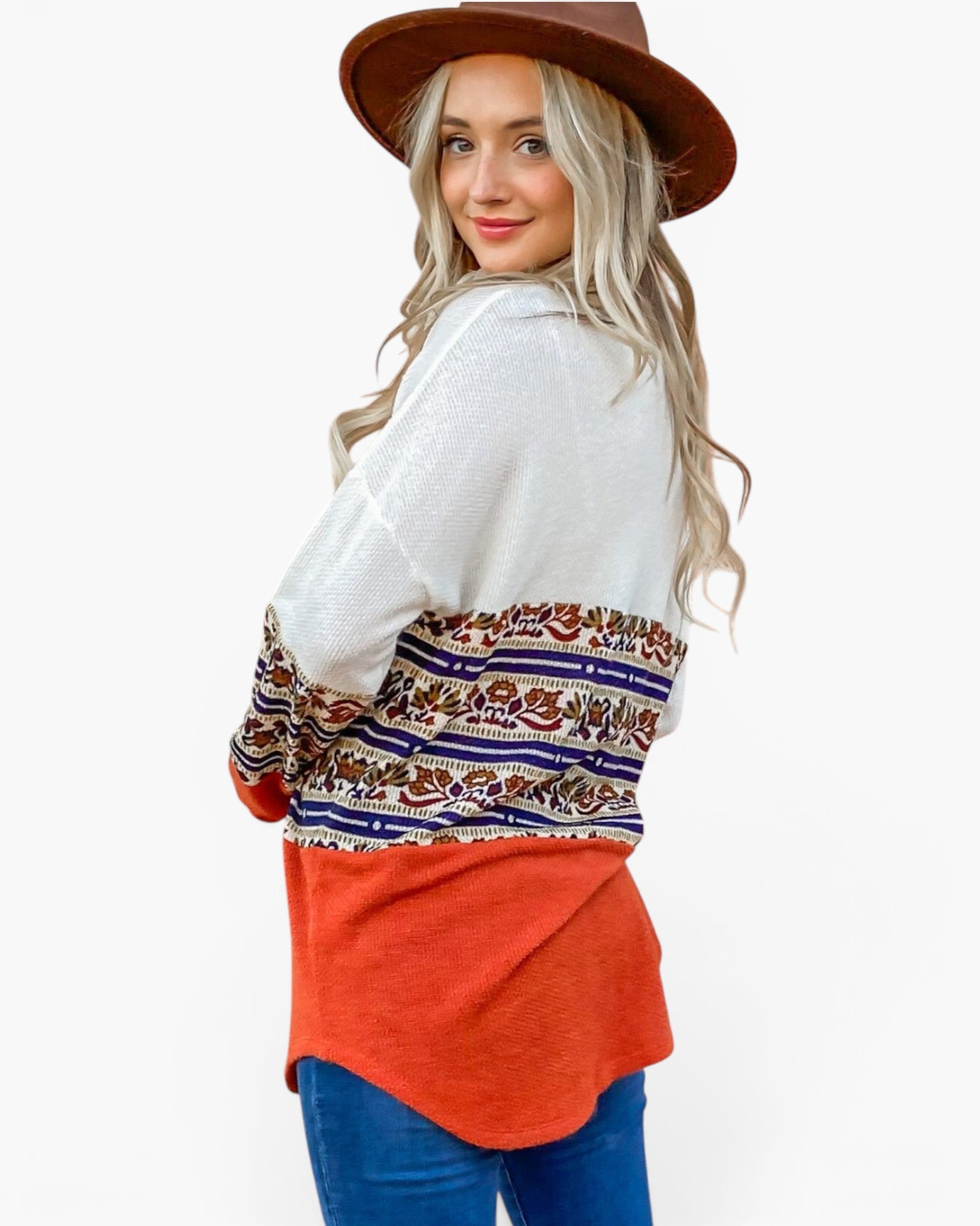 A woman wearing a white knit cardigan with a colorful bohemian patterned band and a bright orange hem, paired with blue jeans and a brown hat, shown from a three-quarters back view against a white background.
