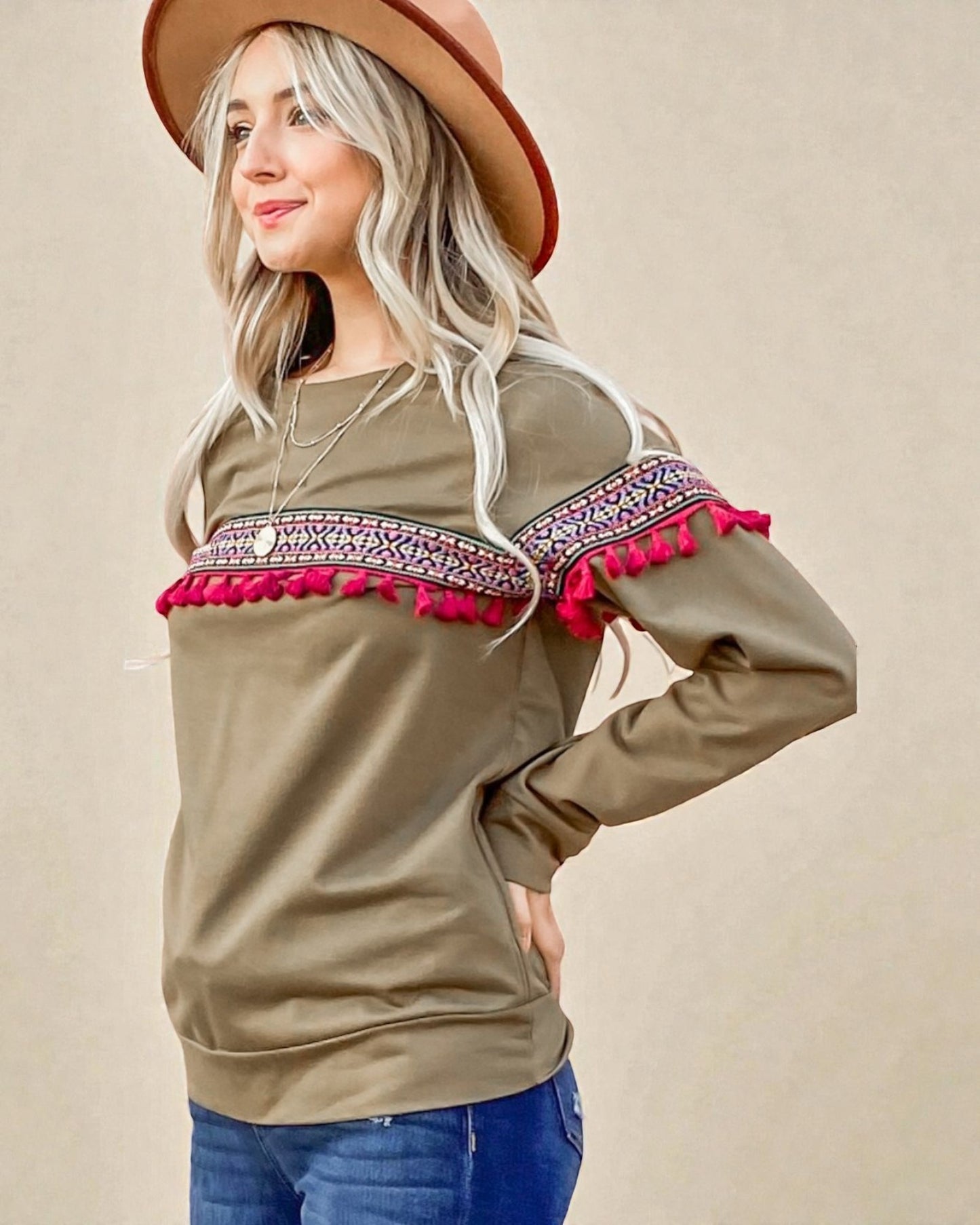 Woman wearing a beige sweater with colorful embroidery and a brown hat on a beige background