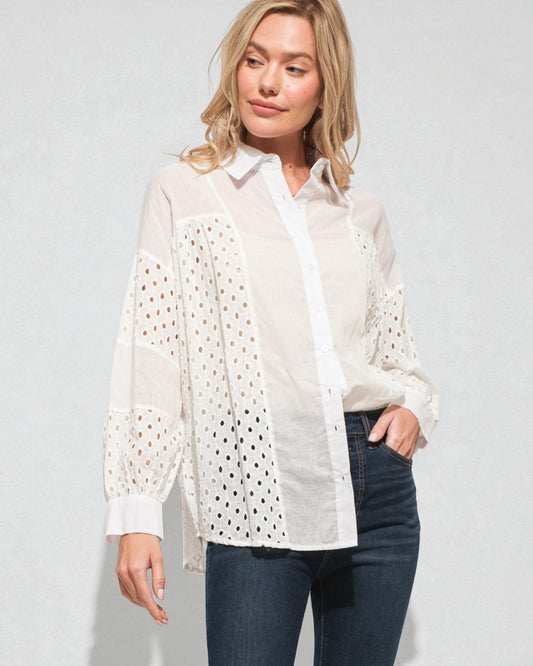 Woman wearing a white lace-trimmed shirt over a plain shirt with blue jeans on a light gray background