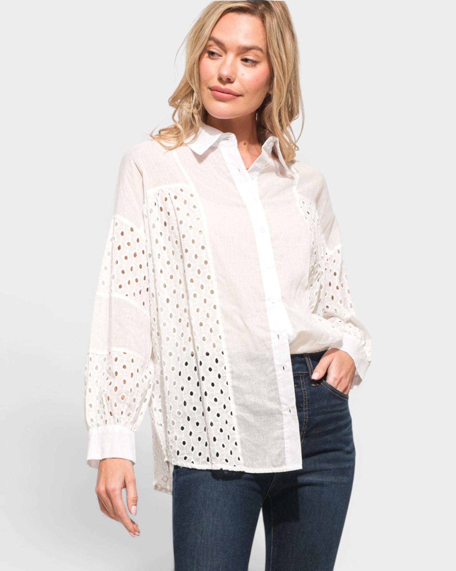 Woman wearing a white blouse with lace details on a plain background