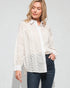 Woman wearing a white lace-trimmed shirt over a plain shirt with blue jeans on a light gray background