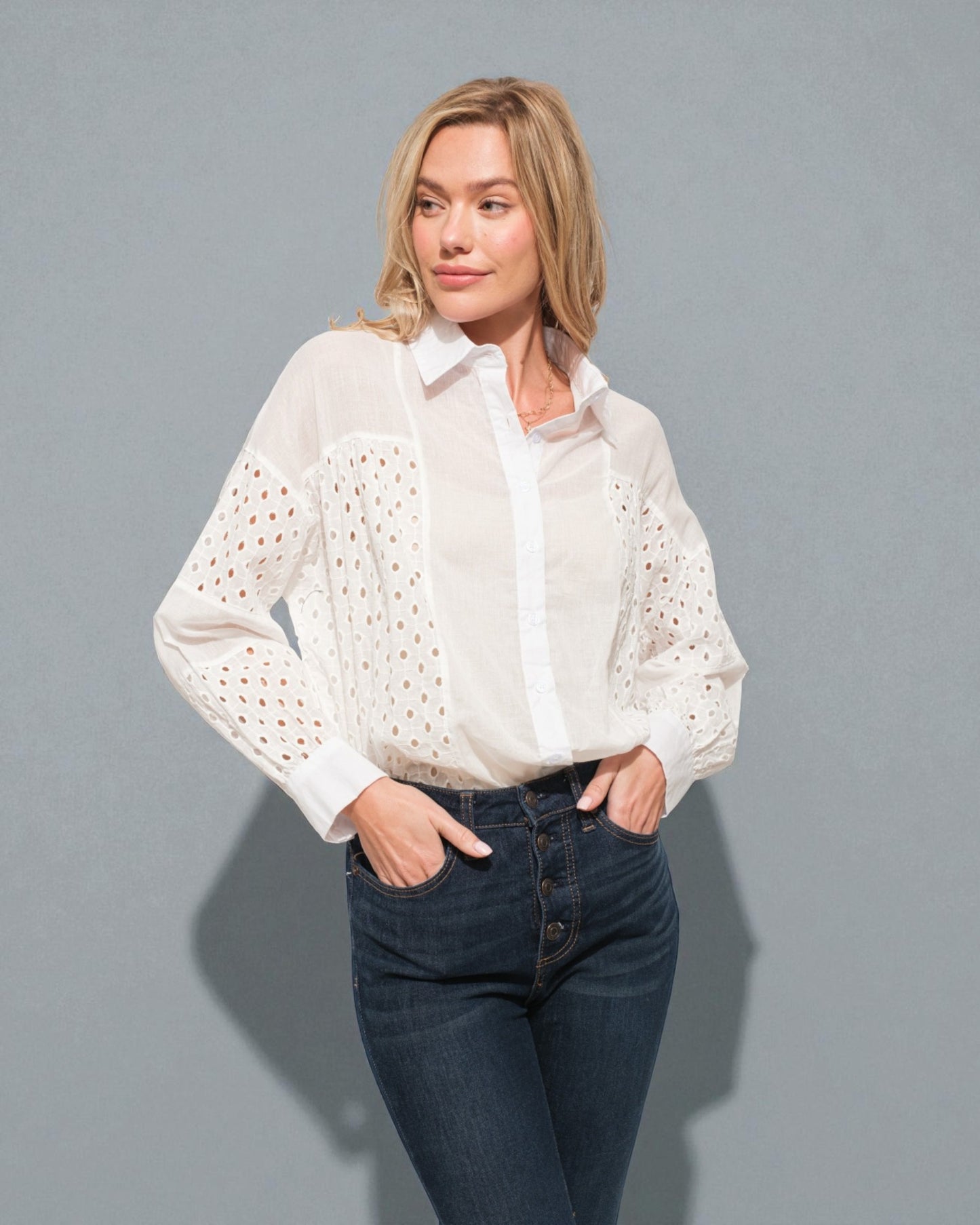 Woman wearing a white blouse with eyelet details and blue jeans against a gray background