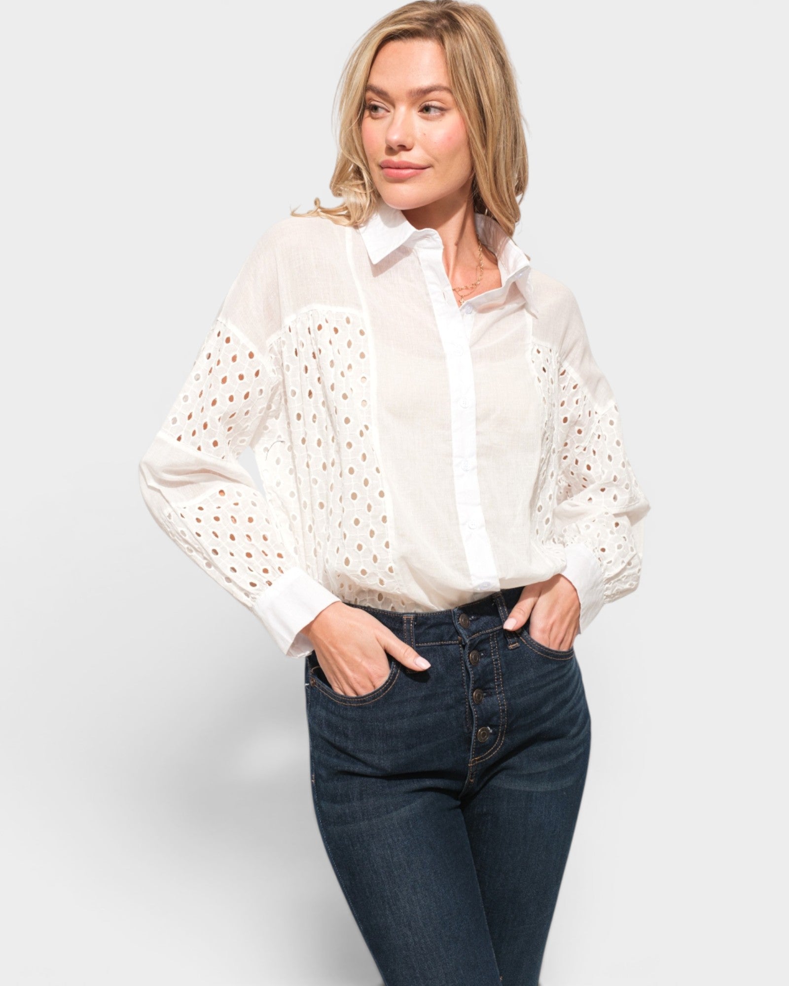 Woman wearing a white blouse with eyelet details and dark jeans on a light gray background