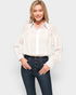 Woman wearing a white blouse with lace details and dark jeans on a plain background
