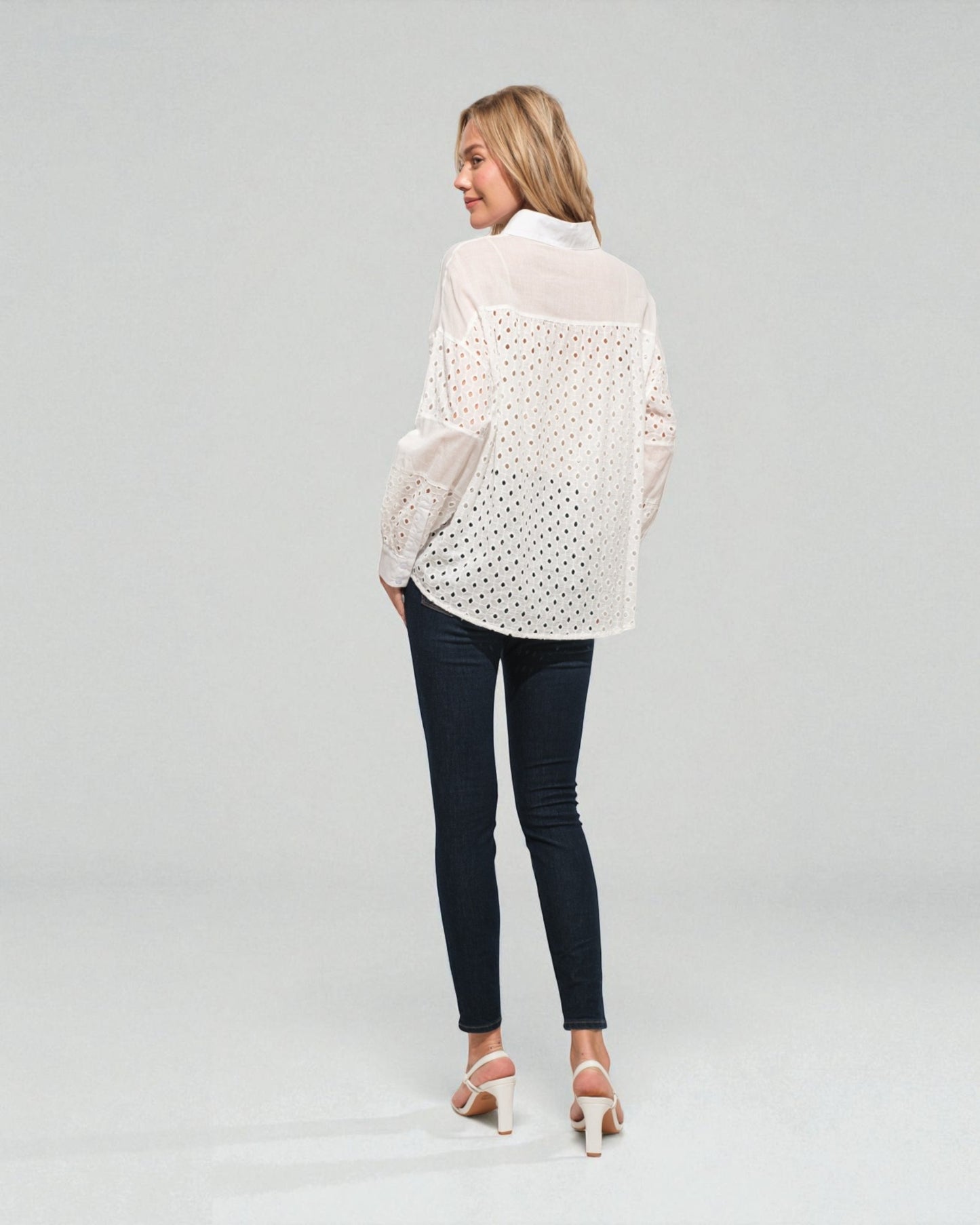 Woman wearing a white lace blouse and dark jeans on a plain background