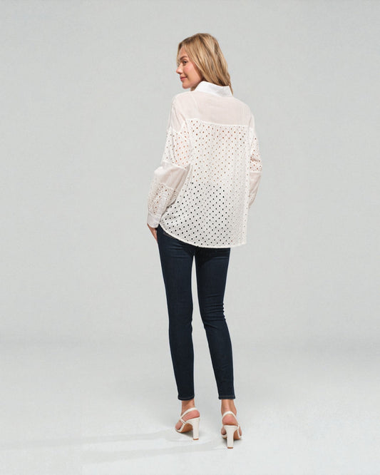 Woman wearing a white lace blouse and dark jeans on a plain background