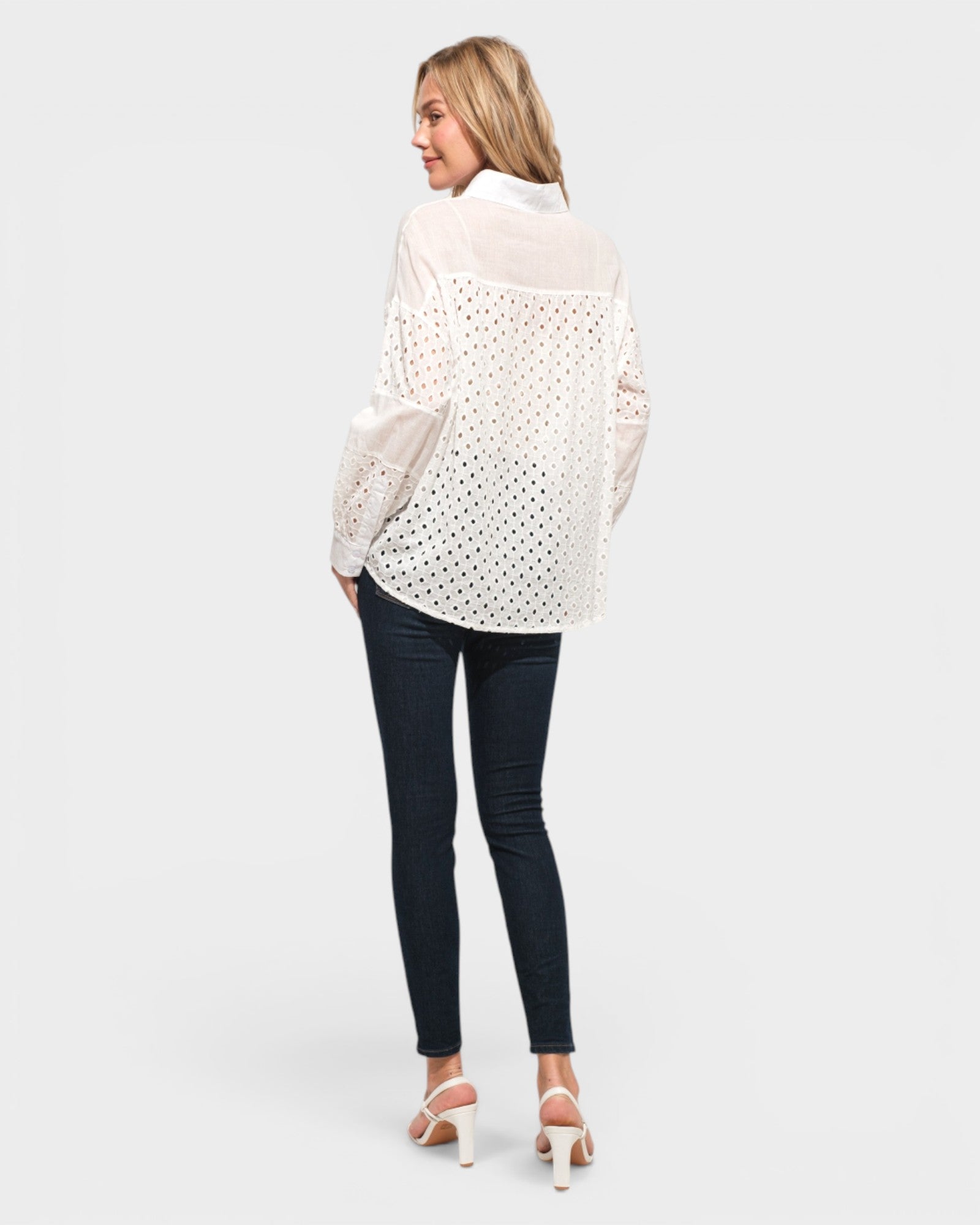 Woman wearing a white polka dot shirt and dark jeans on a plain background