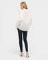 Woman wearing a white polka dot shirt and dark jeans on a plain background