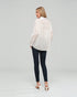 Woman wearing a white lace blouse and dark jeans on a plain background