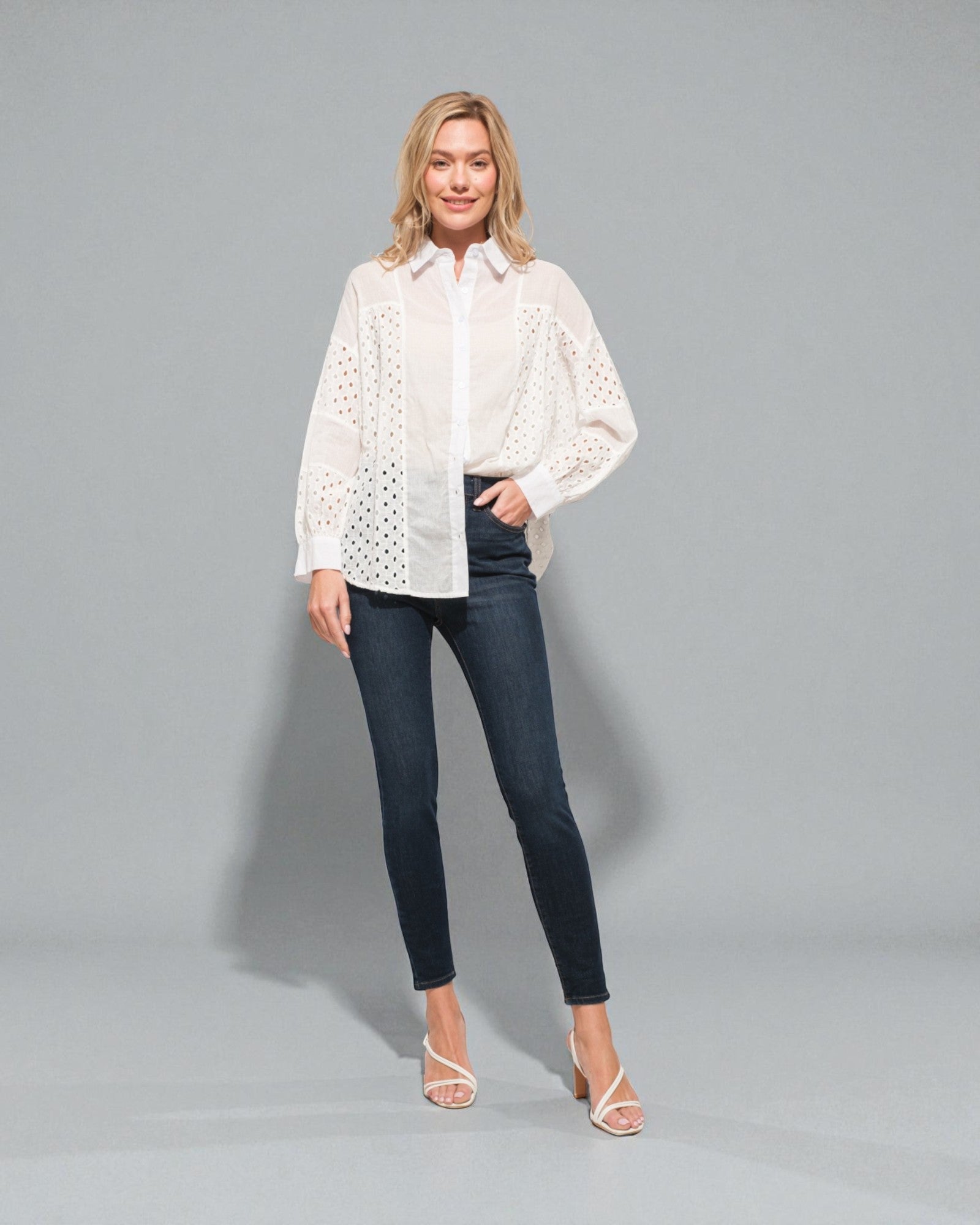 Woman wearing a white blouse with lace details and dark jeans on a gray background