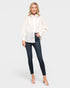 Woman wearing a white blouse with polka dots and dark jeans on a plain background