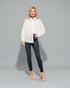 Woman wearing a white blouse with lace details and dark jeans on a gray background