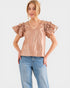 Woman wearing a beige blouse with ruffled sleeves and blue jeans on a white background
