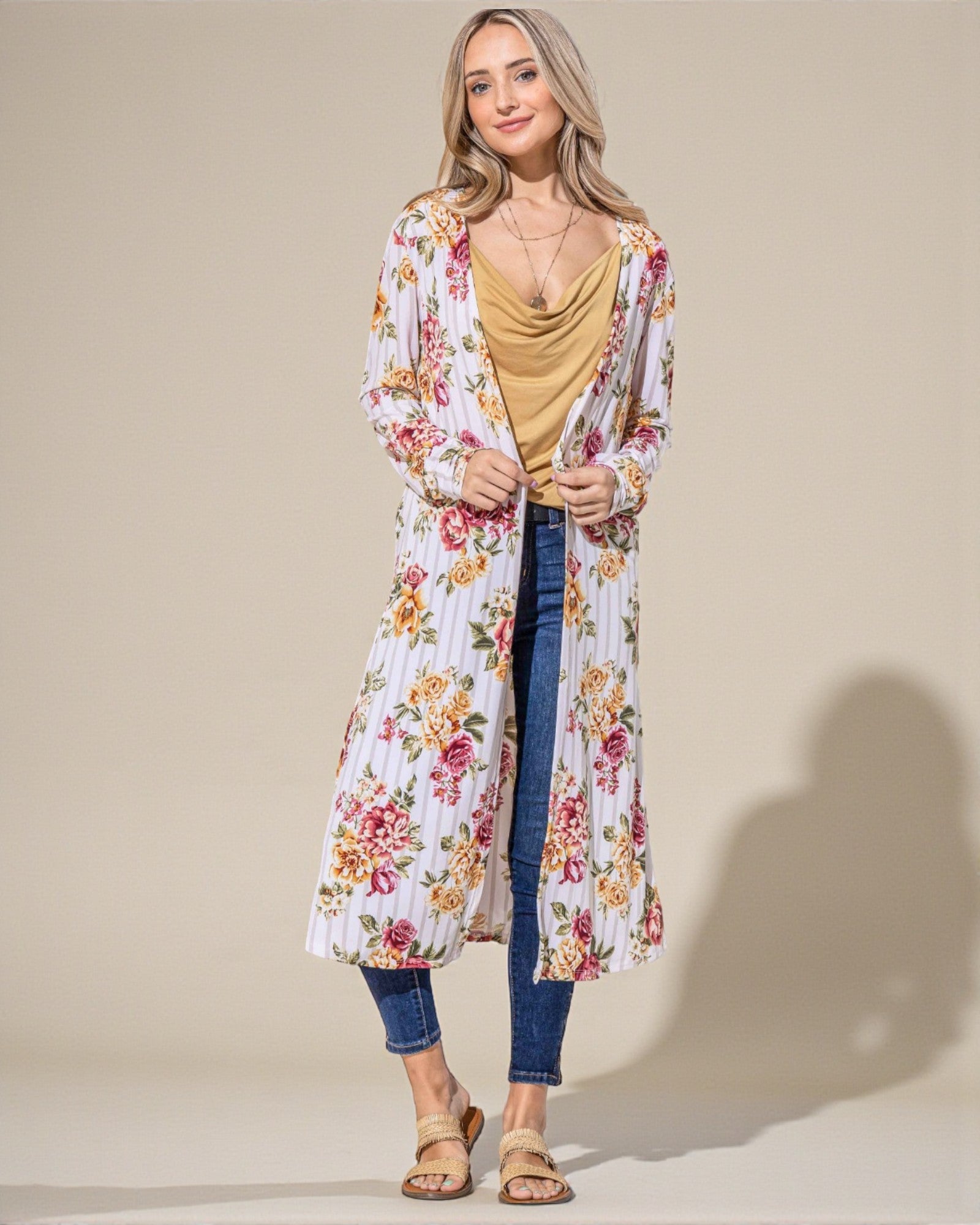 Woman wearing a floral kimono over a mustard top and blue jeans on a beige background