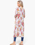A woman shown from the back wearing a long-sleeve floral tunic dress with vertical pleats, paired with blue jeans and tan slide sandals, against a plain white background.