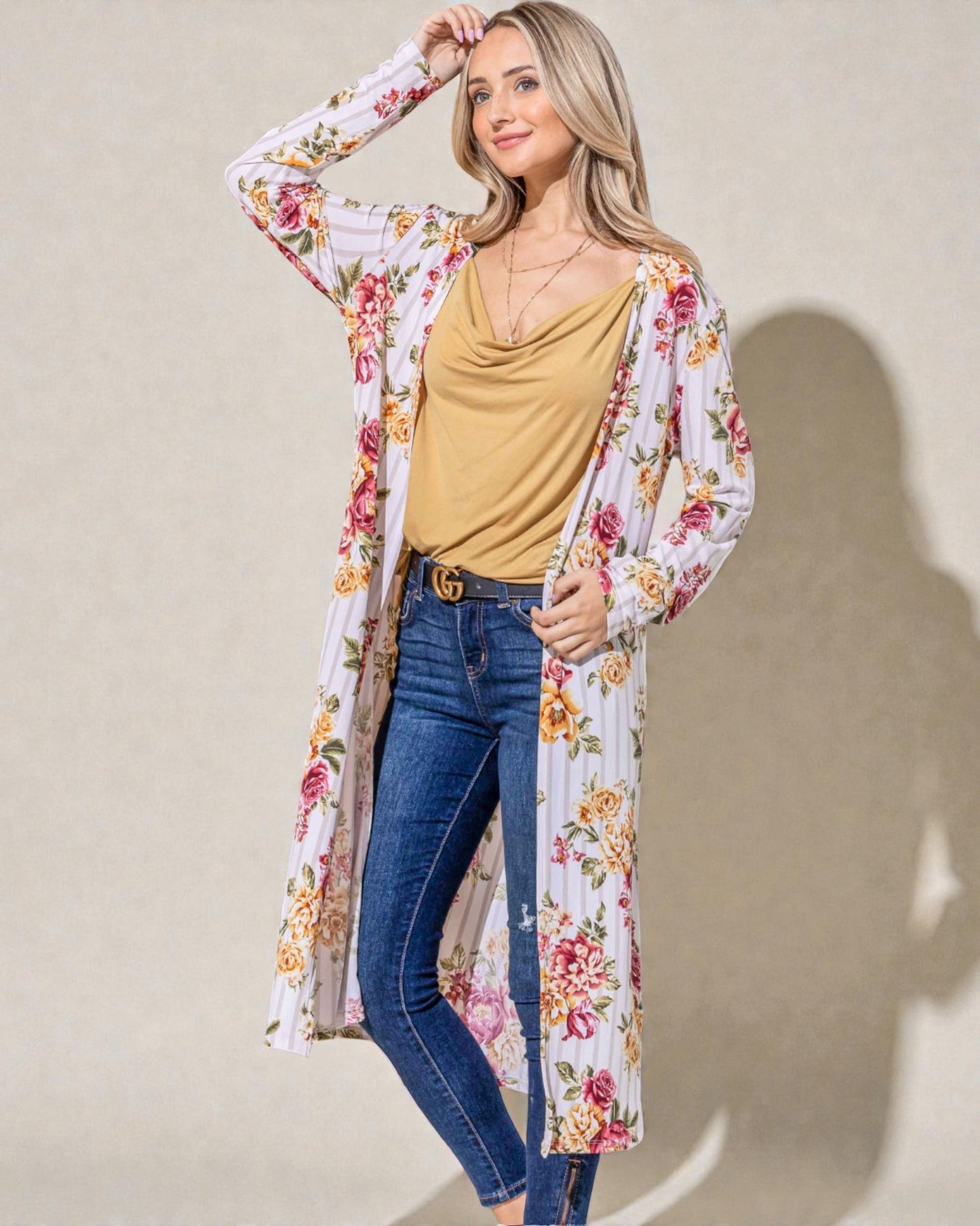 Woman wearing a floral kimono over a yellow top and blue jeans against a beige background
