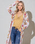 Woman wearing a floral kimono over a yellow top and blue jeans on a plain background
