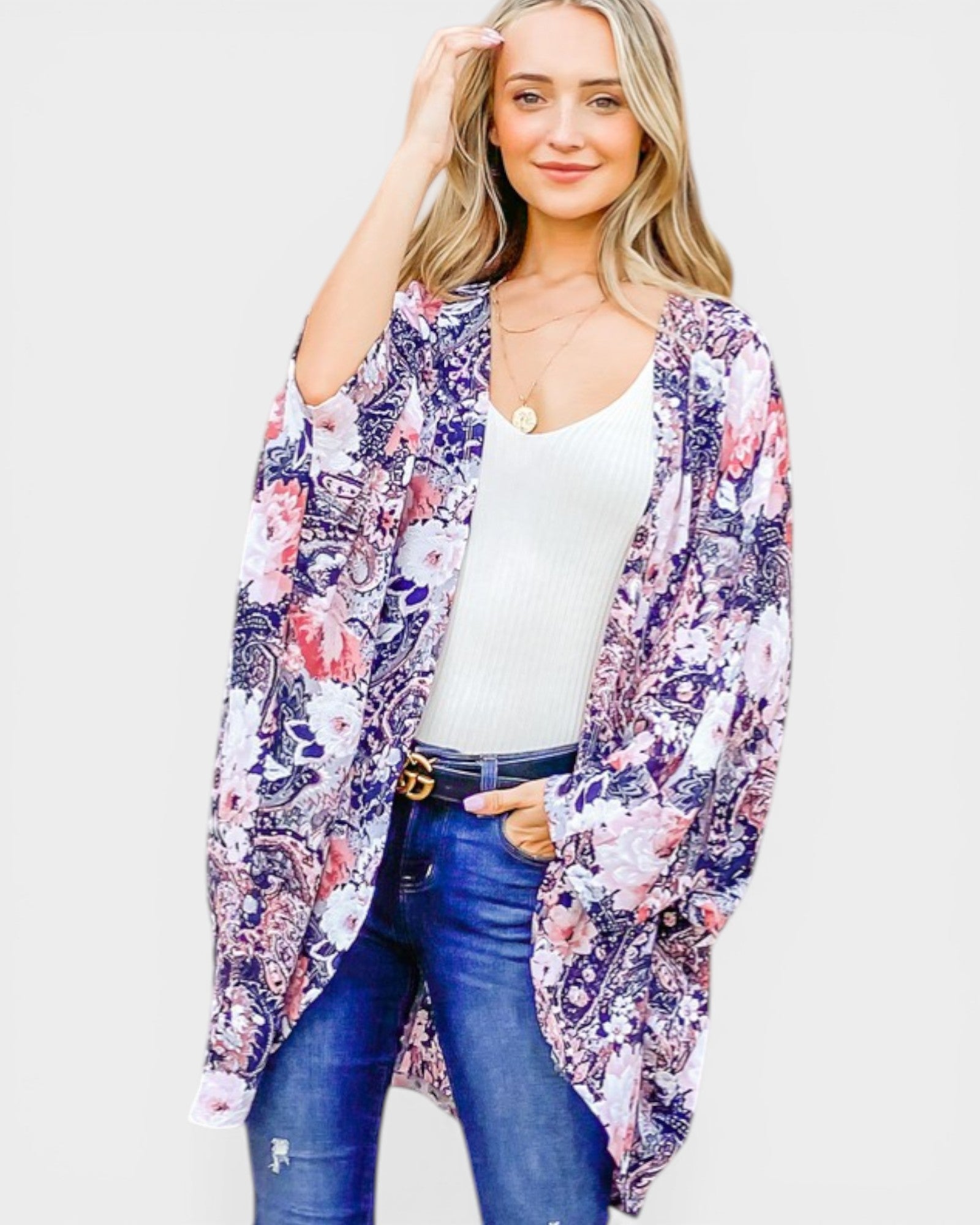 Woman wearing a floral kimono over a white top and blue jeans on a light gray background