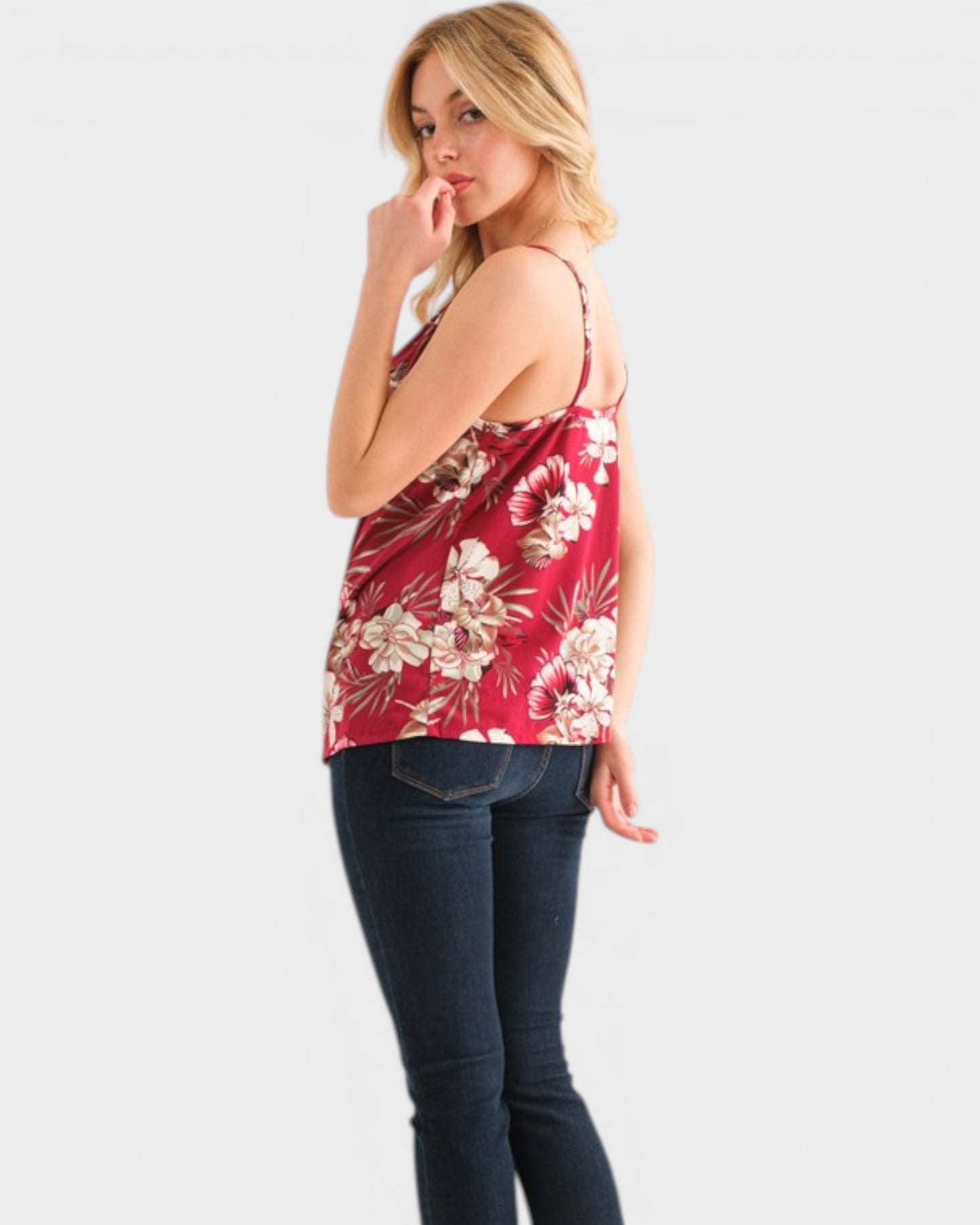 Woman wearing a red floral top and dark jeans on a white background