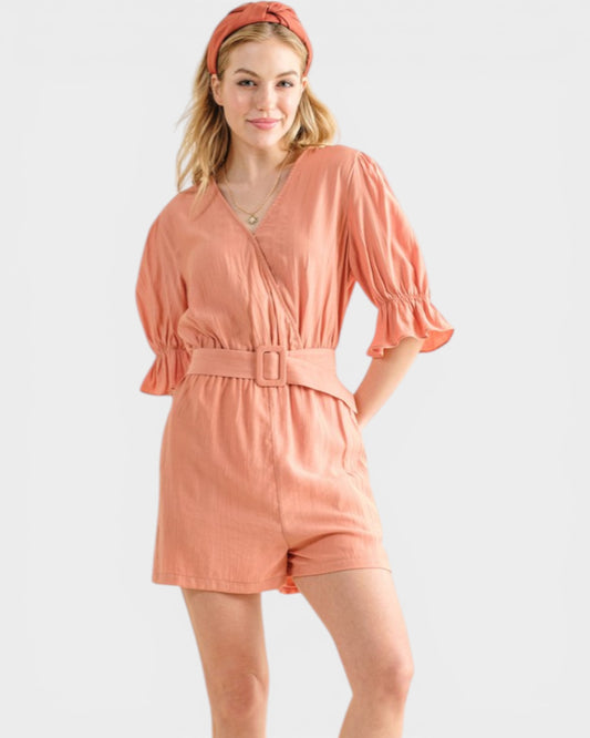 Woman wearing a peach-colored romper with a belt on a white background