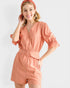 Woman wearing a peach-colored romper with a matching headscarf on a white background