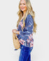 Woman wearing a blue floral blouse and holding a woven bag on a white background