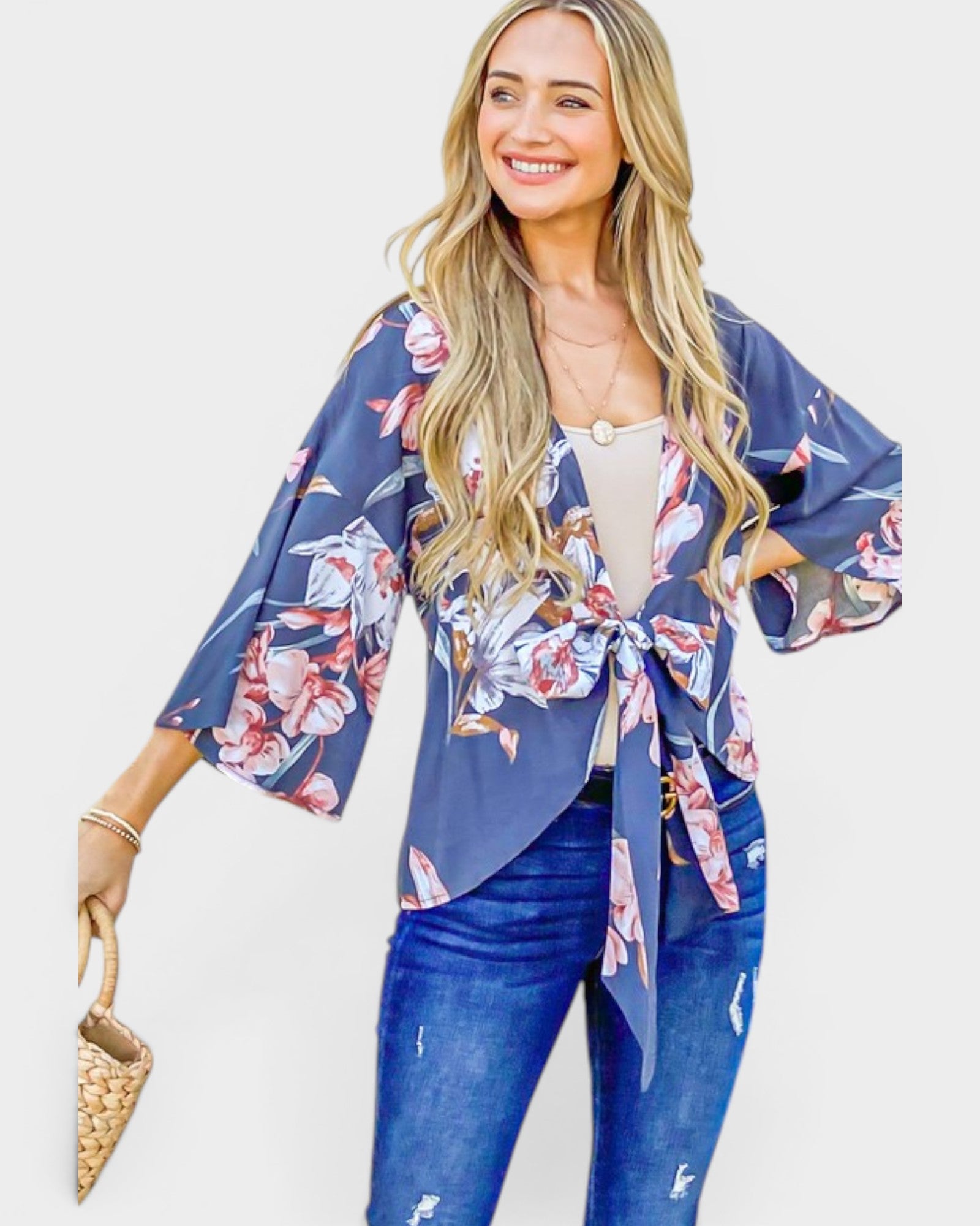Woman wearing a blue floral kimono over a white top and jeans, holding a woven handbag.