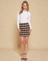 Woman wearing a white turtleneck and plaid skirt against a beige background