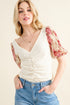 Woman wearing a cream top with floral sleeves and blue jeans on a beige background