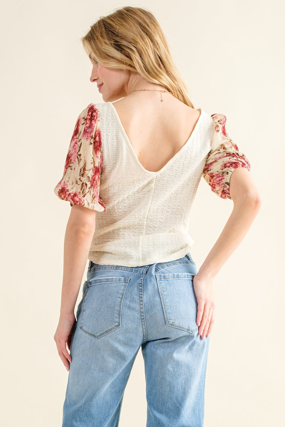 Woman wearing a white top with floral sleeves and blue jeans on a beige background