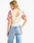 A woman shown from the back wearing a cream-colored textured knit top with red and beige floral puff sleeves, paired with light blue jeans, against a plain white background.