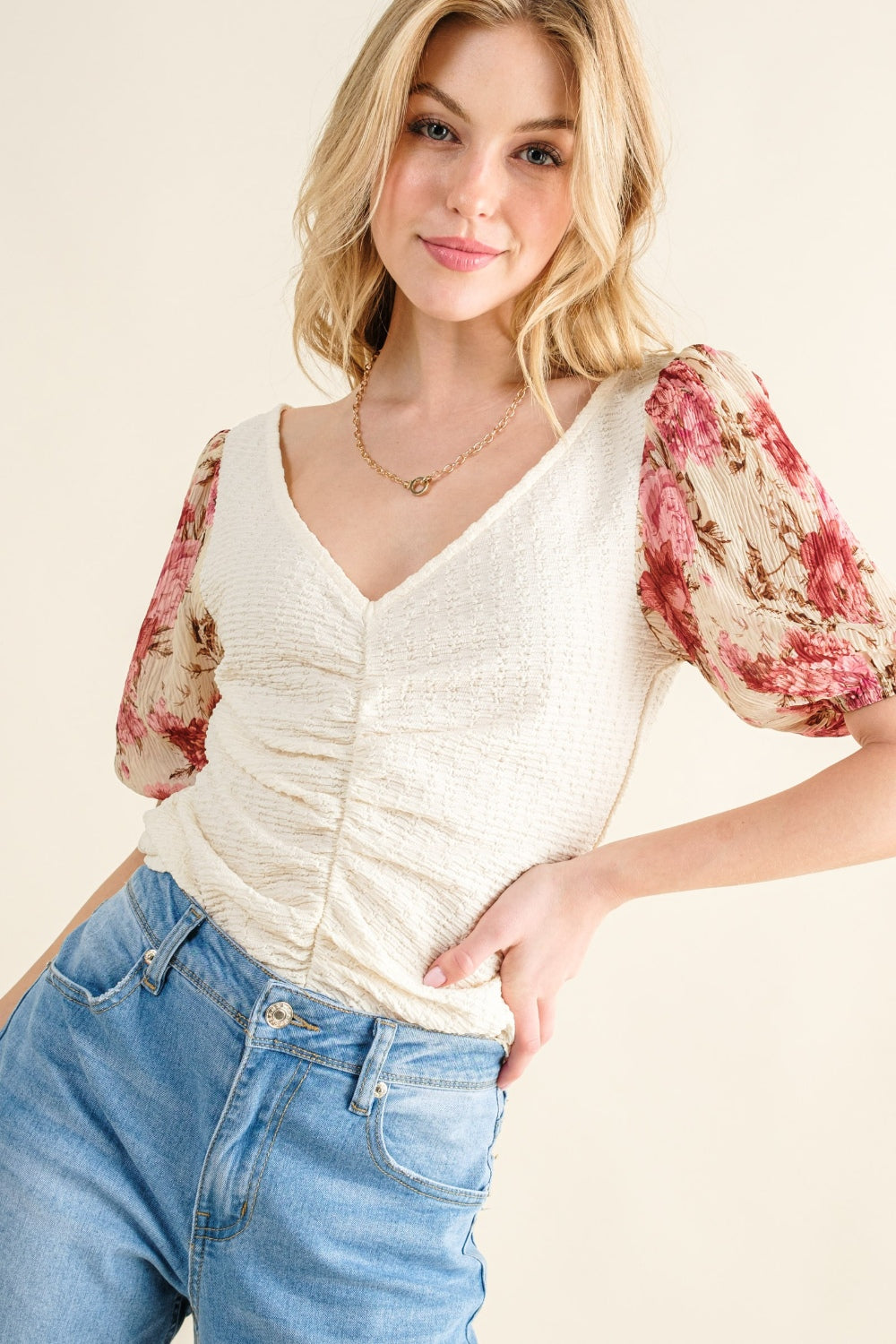 Woman wearing a white top with floral sleeves and blue jeans on a plain background