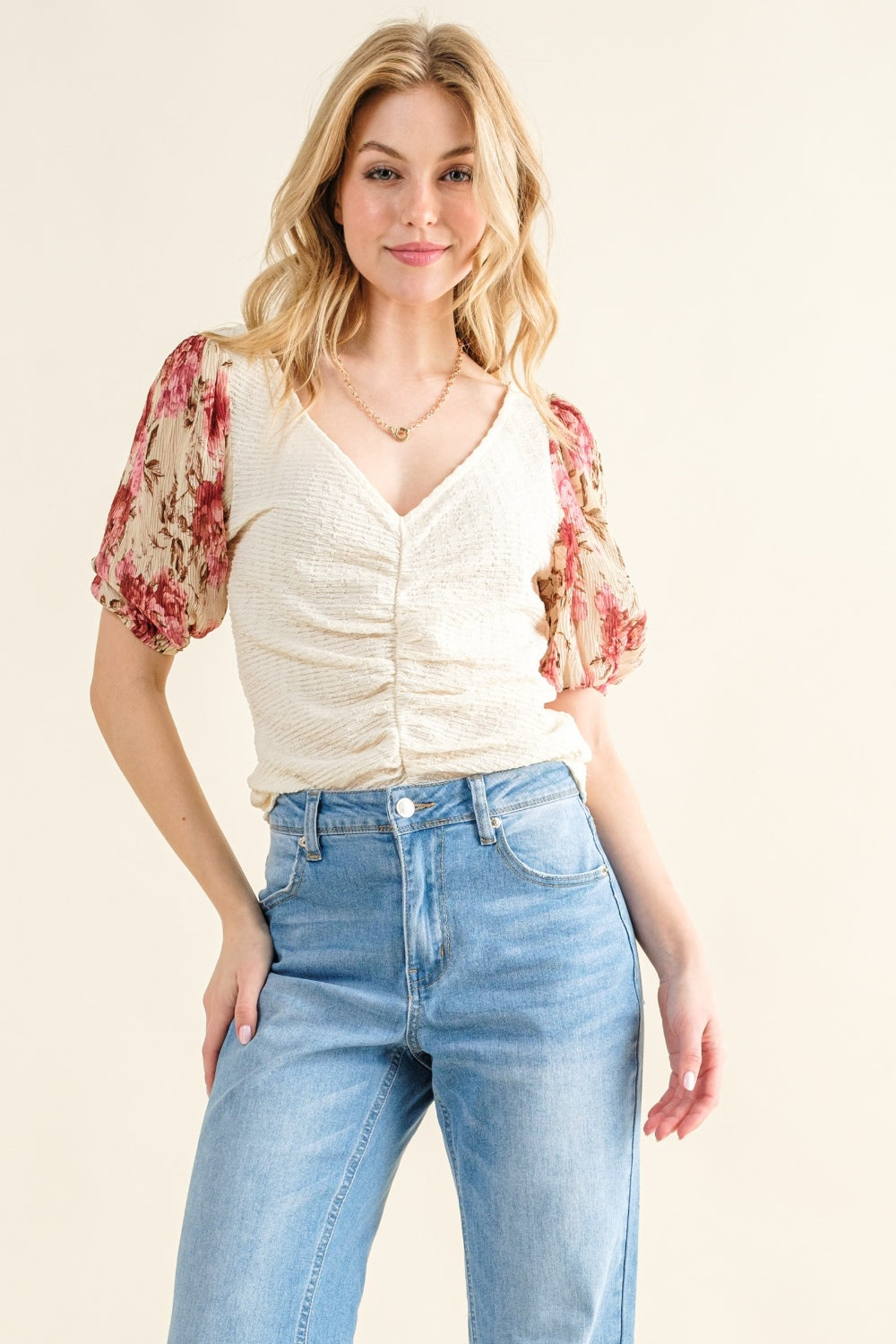 Woman wearing a floral blouse with short sleeves and high-waisted jeans on a beige background