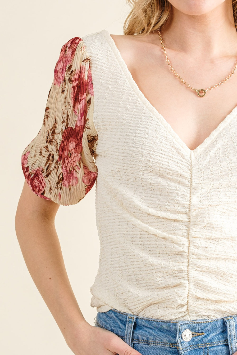 Woman wearing a white top with floral sleeves and blue jeans on a beige background