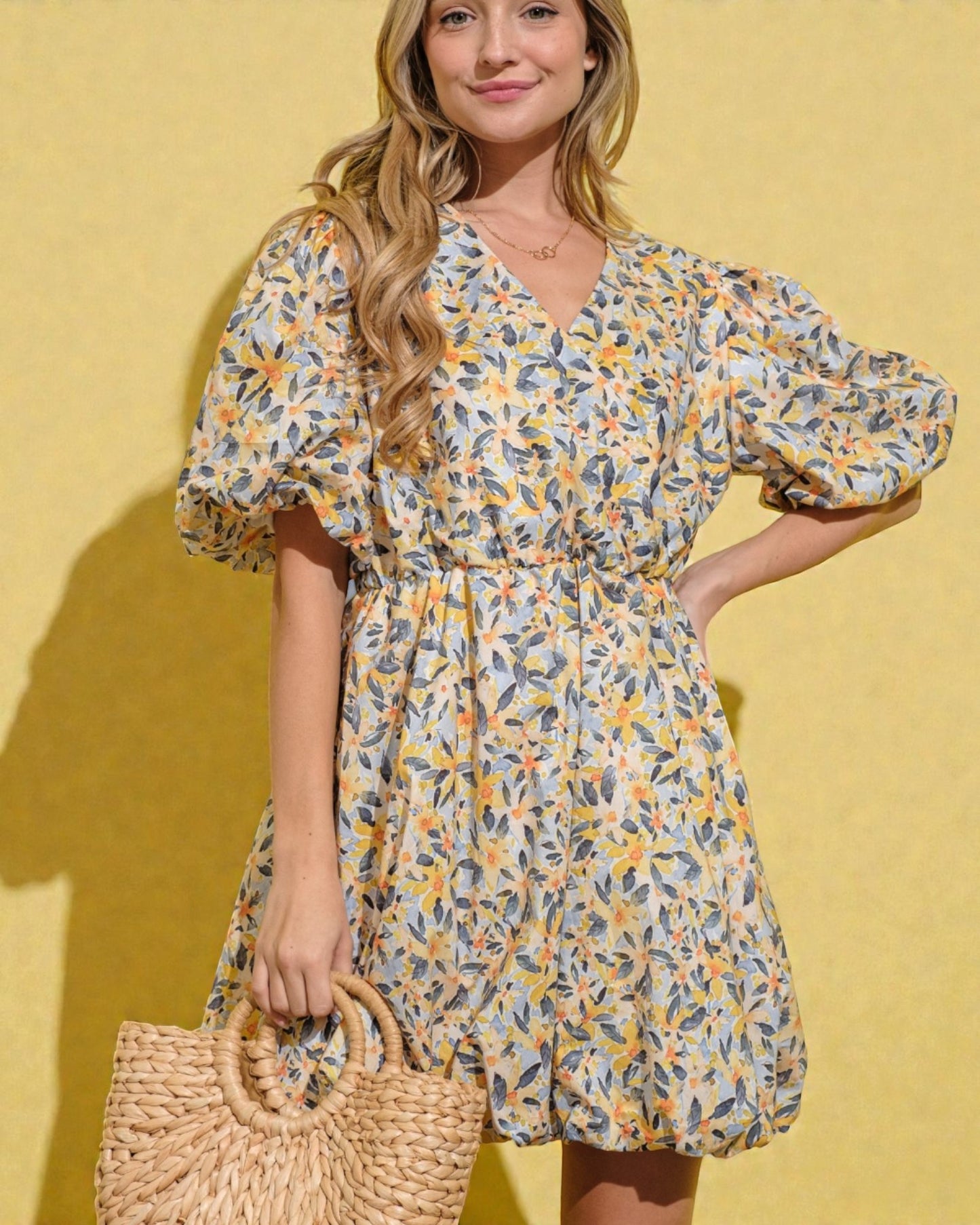 Woman wearing a floral dress holding a straw bag against a yellow background