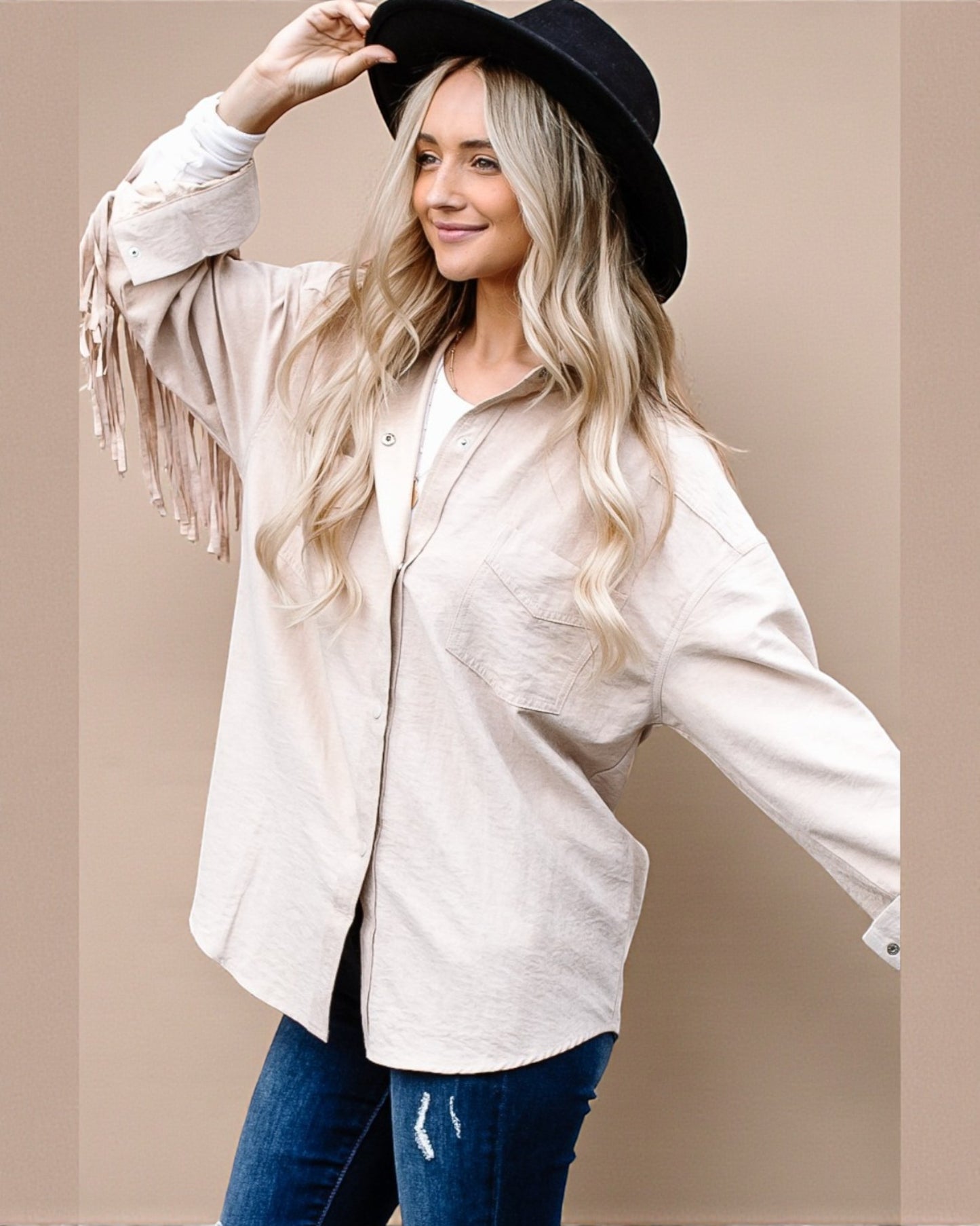 Woman wearing a beige fringed jacket and black hat on a beige background