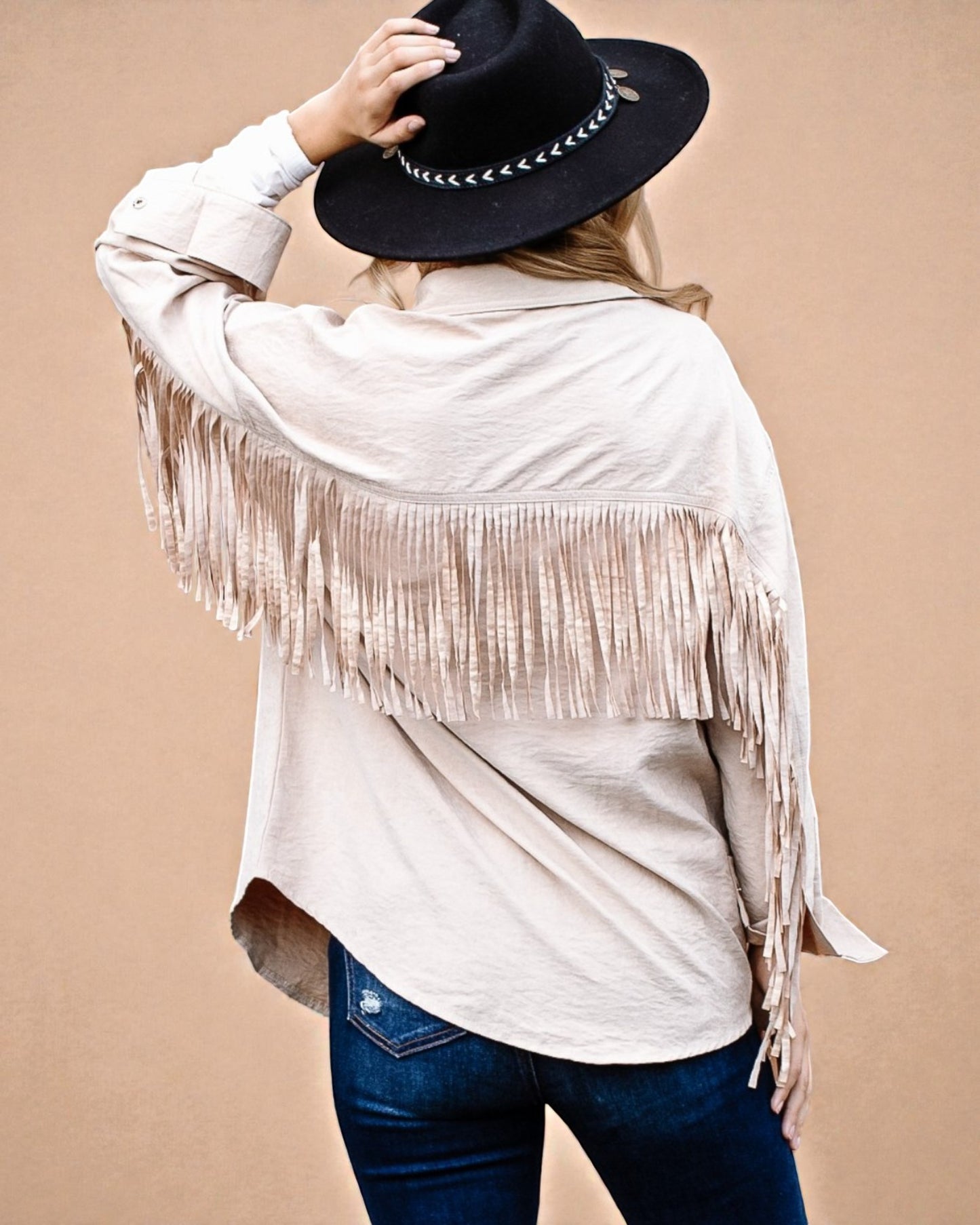 Person wearing a beige fringe jacket and black hat on a beige background
