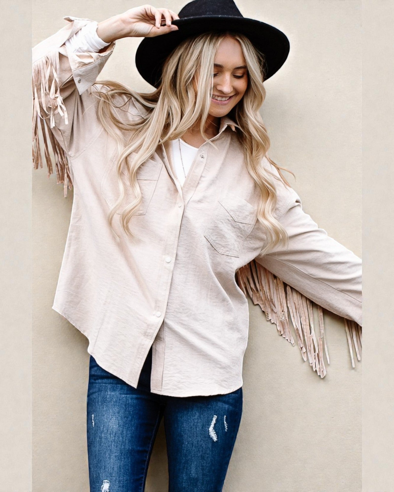 Woman wearing a white fringed shirt and black hat against a beige background