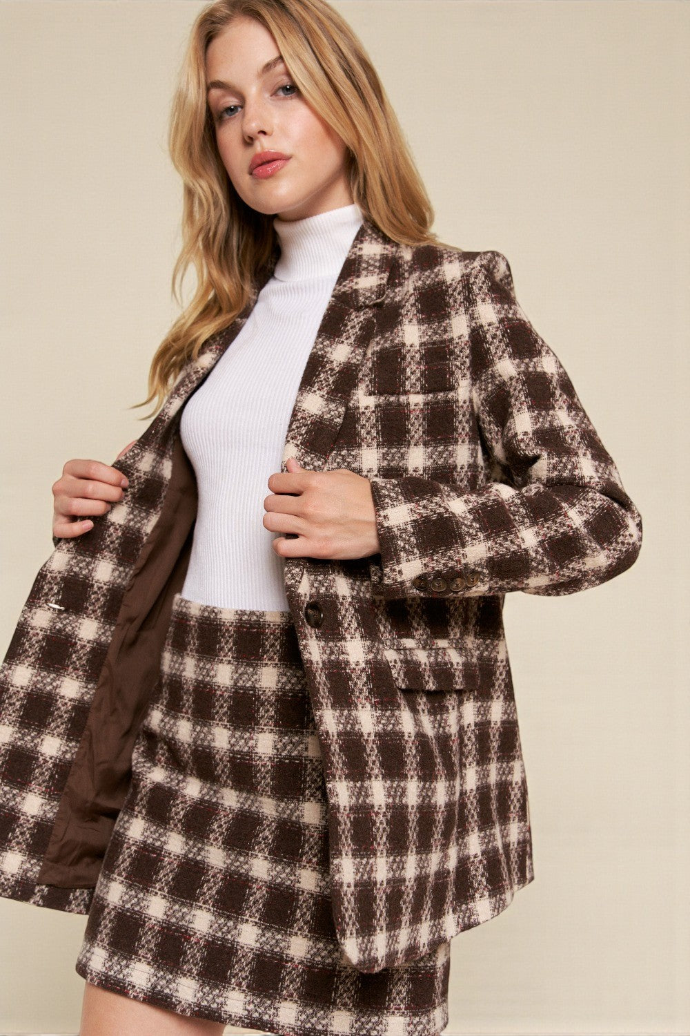 Woman wearing a brown and beige checkered coat against a plain background