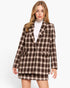 A woman modeling a brown and beige plaid blazer and matching mini skirt over a white turtleneck, shot against a plain white studio background.
