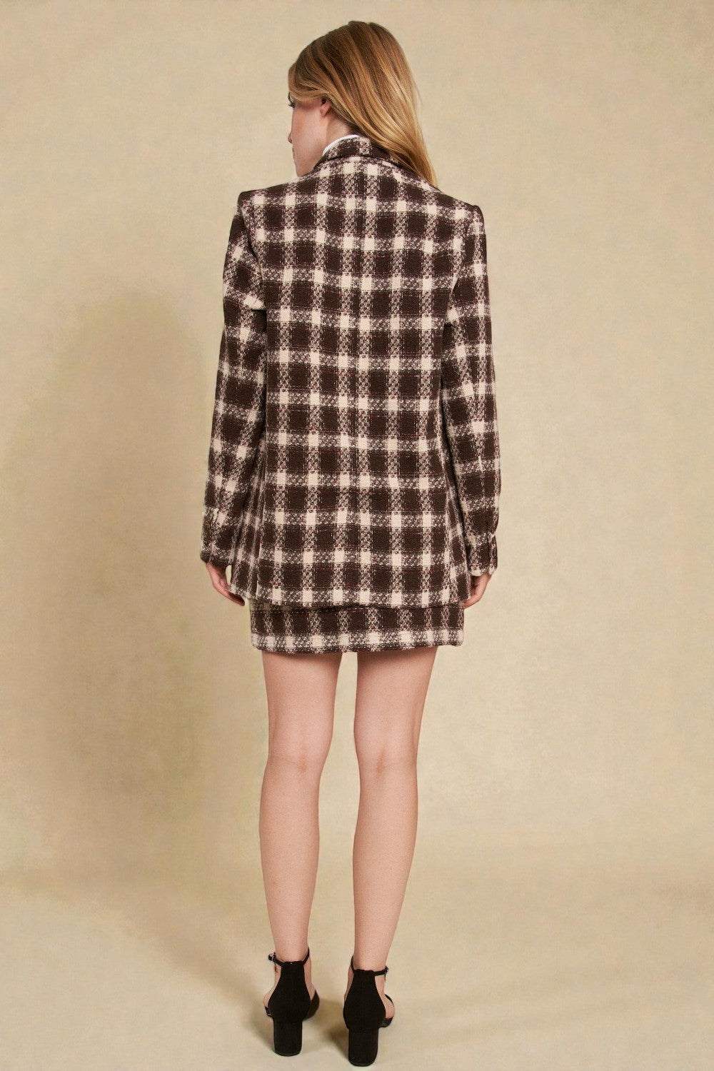 Person wearing a plaid blazer and skirt set on a beige background