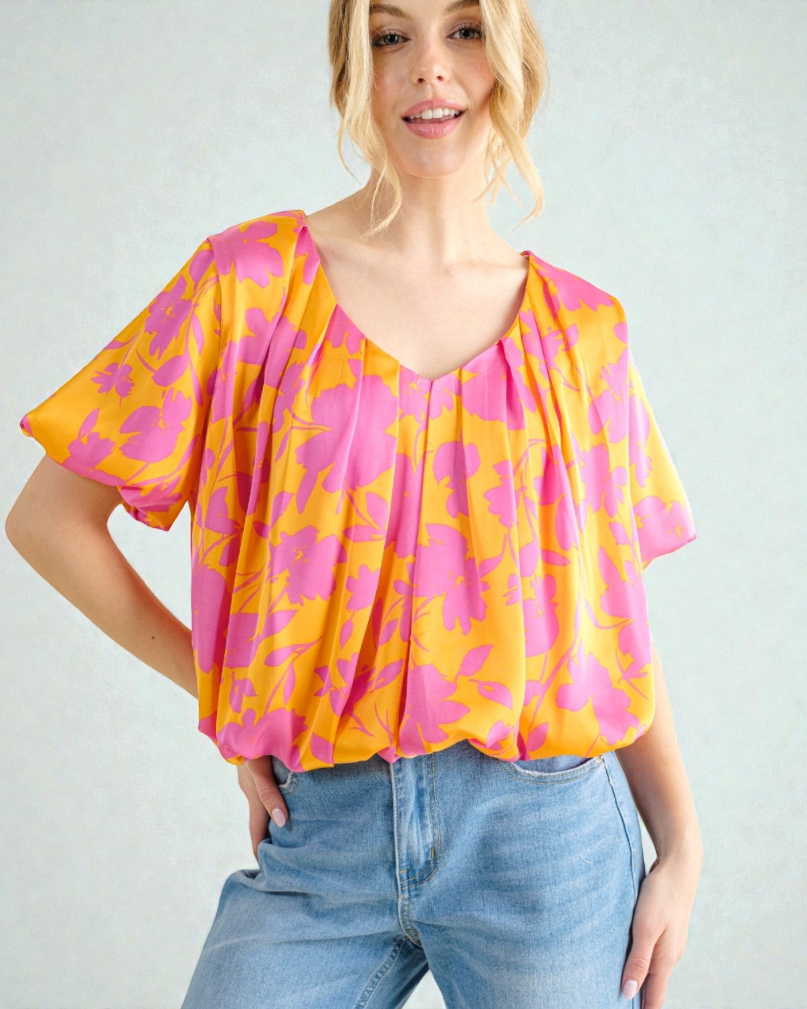 Woman wearing a pink and orange floral blouse with blue jeans on a light gray background