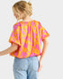 A woman shown from the back wearing a bright yellow and pink patterned short-sleeve blouse with light blue jeans, against a light gray studio background.