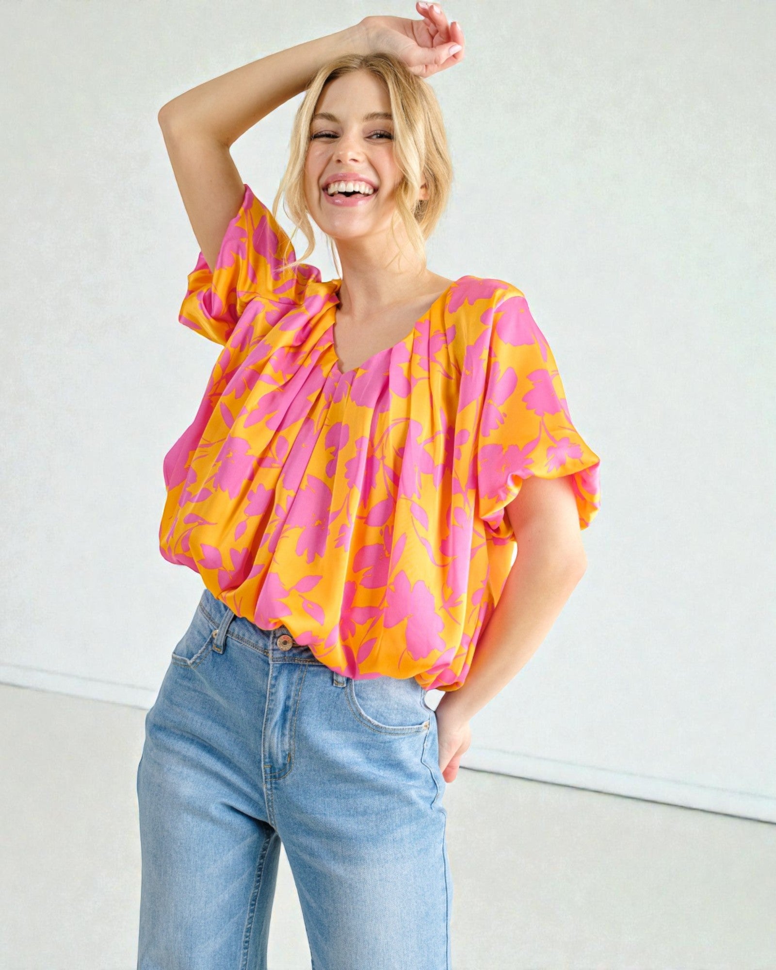 Woman wearing a colorful blouse and jeans against a plain background