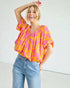 Woman wearing a colorful blouse and jeans against a plain background